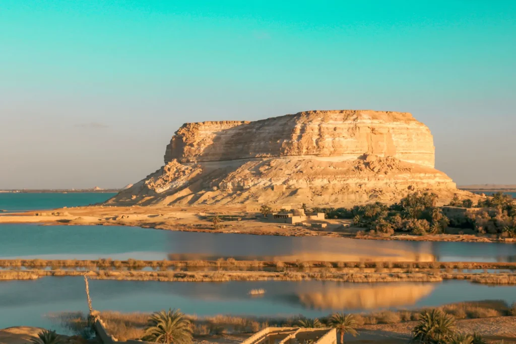 how to get to Siwa Oasis: Turquoise lake beneath desert cliffs in Siwa Oasis