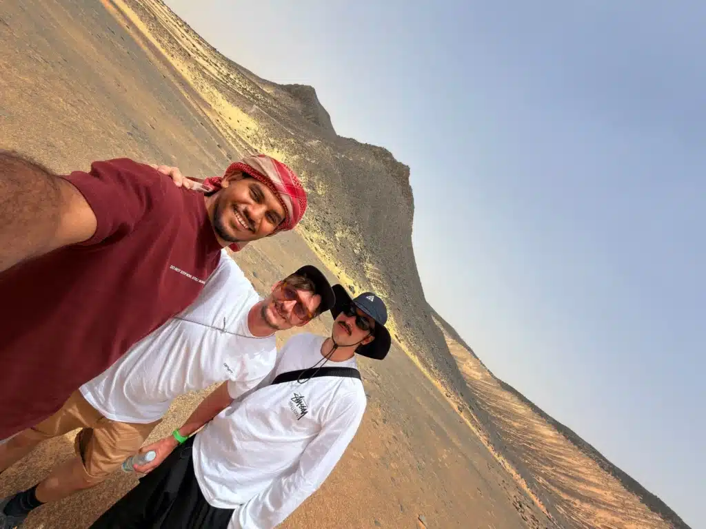 Three people take a selfie in front of a dark volcanic hill in Egypt's Black Desert.